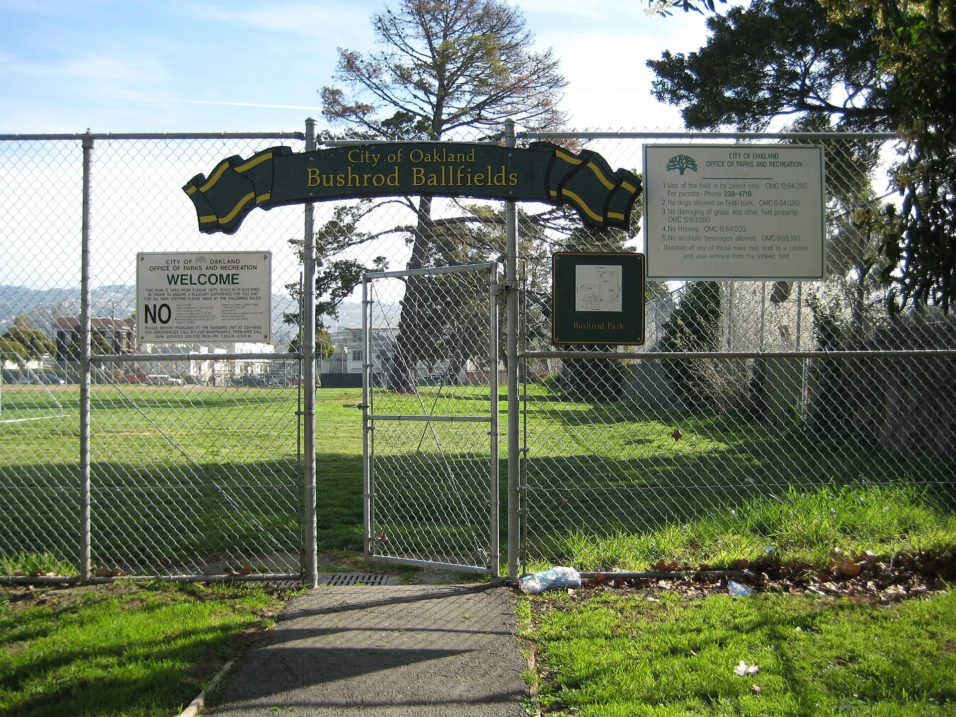 A chain-link gate with a green arched sign reading City of Oakland Bushrod Ballfields