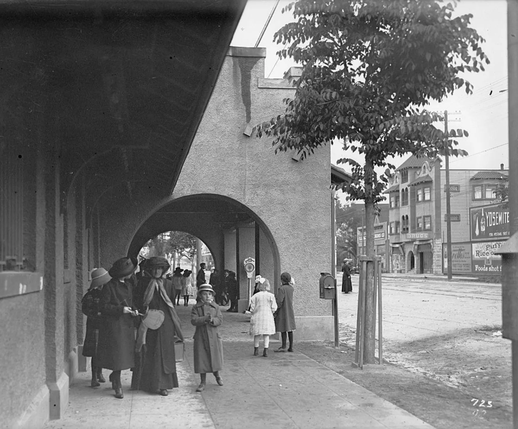 Black-and-white photo of women and children in long coats and hats under the arched Telegraph Avenue entrance to Idora Park