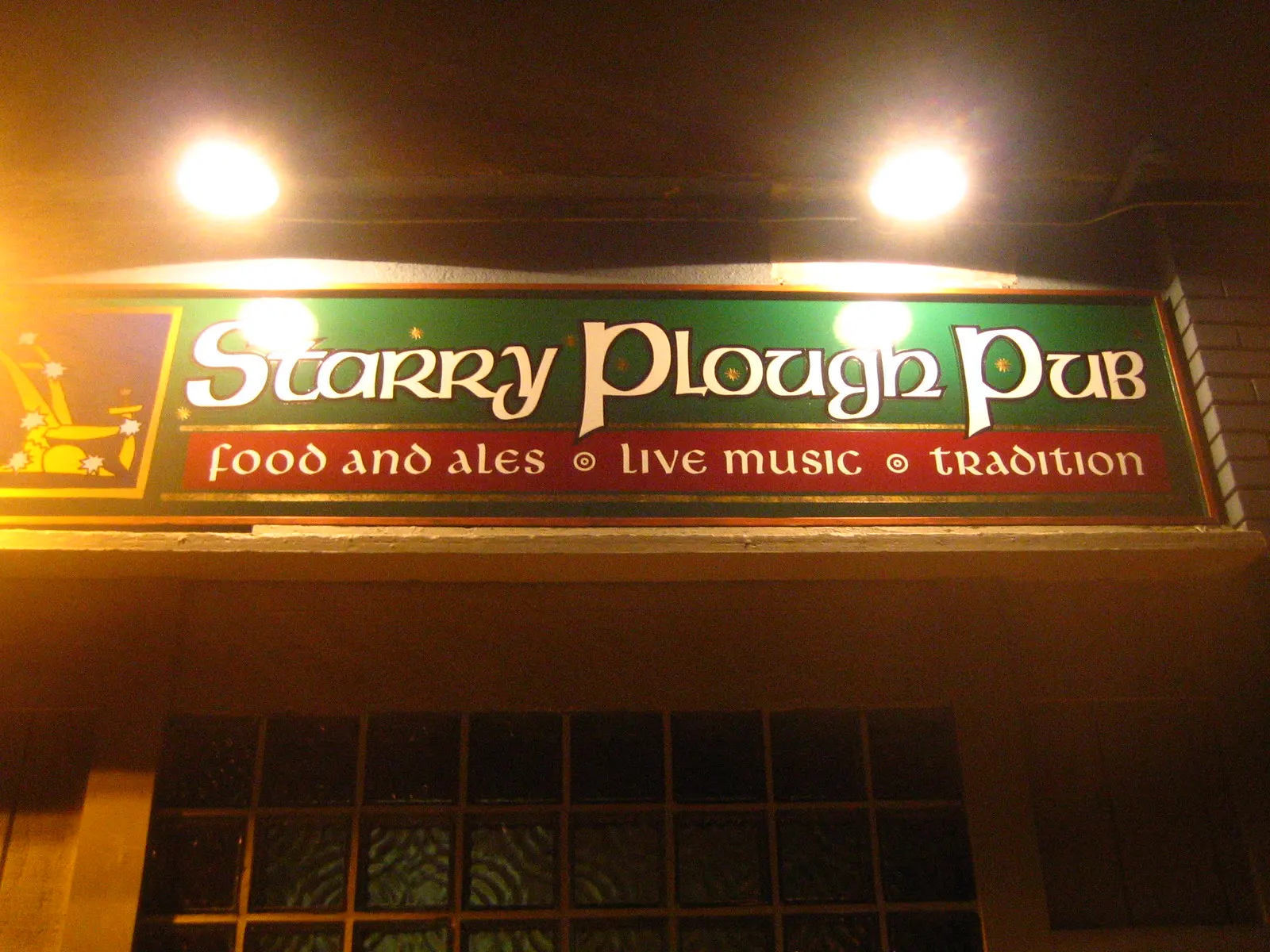The illuminated Starry Plough Pub sign at night reading food and ales, live music, tradition