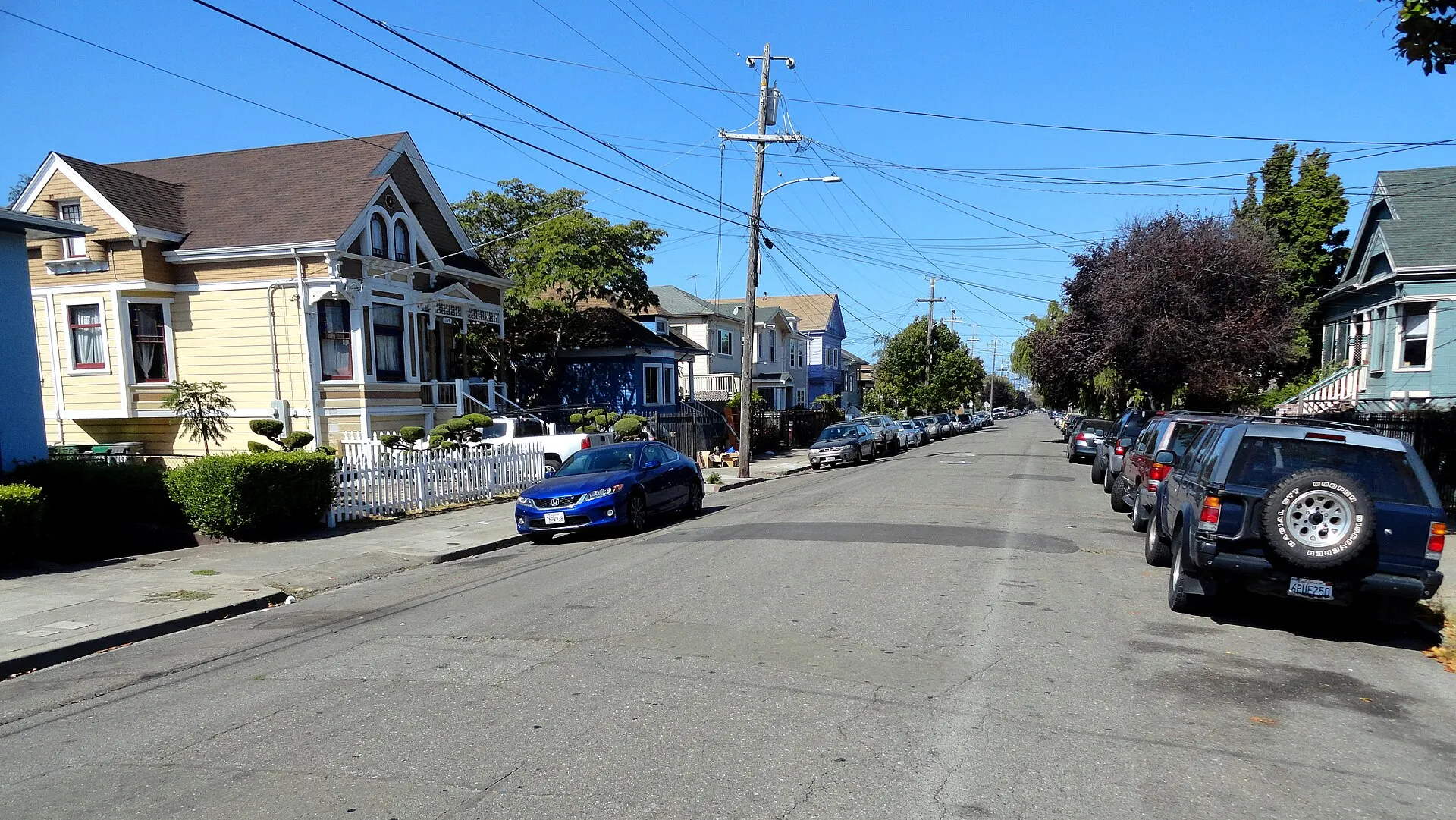 A sunny residential street lined with Victorian and Craftsman houses